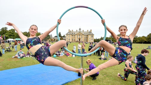 Two gymnasts hang on either side of a hoop with Belton House framed in its centre.